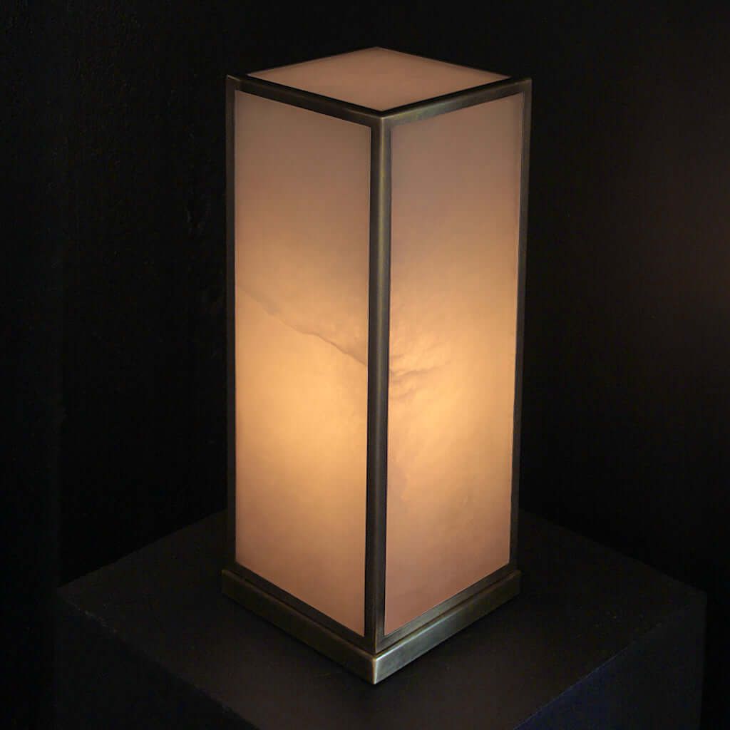 Alabaster stone table lamp on a wooden nightstand next to a bed with pillows and blankets.