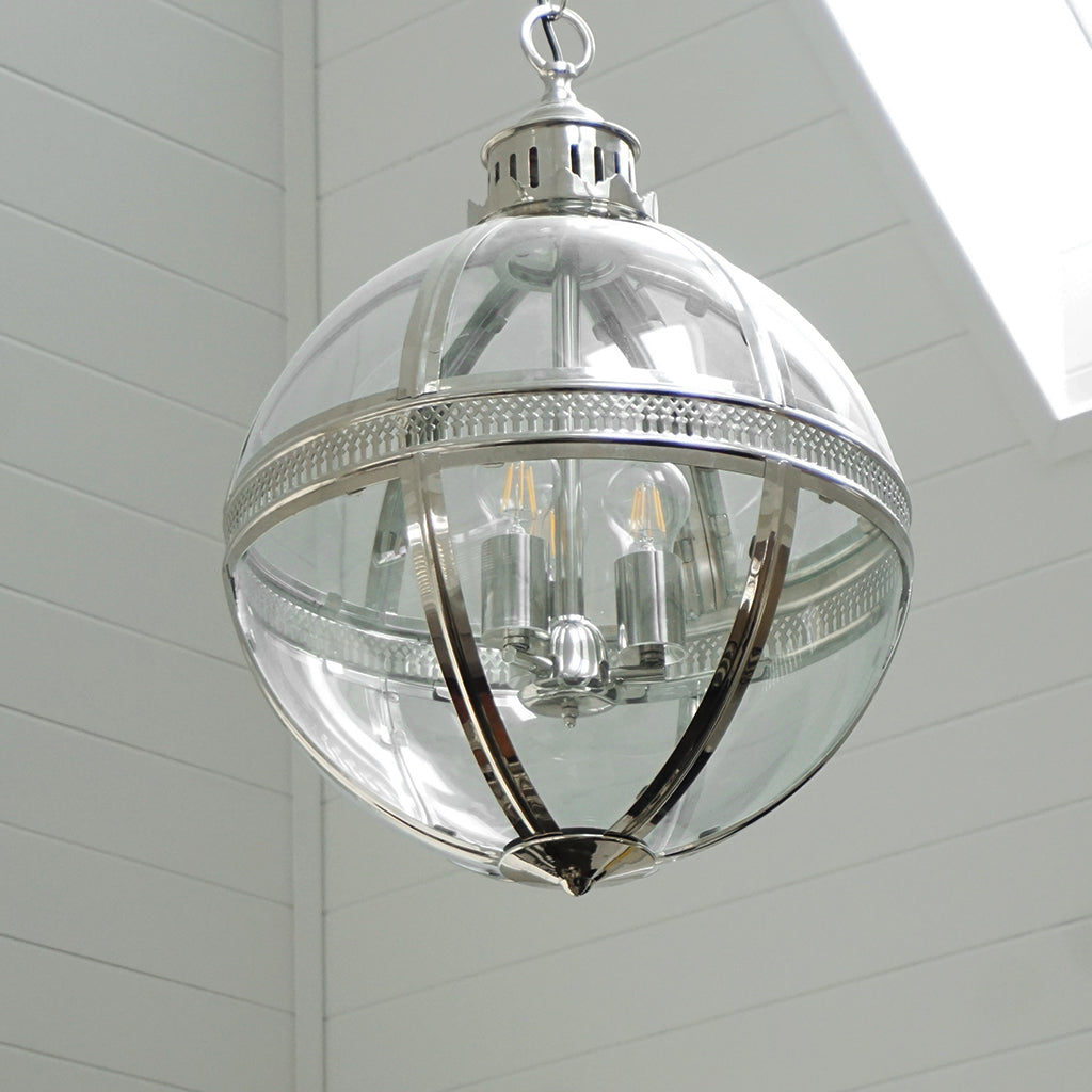 A spherical pendant chandelier with a polished silver metal frame and clear glass , hanging from a ceiling with white shiplap panels and a skylight visible.