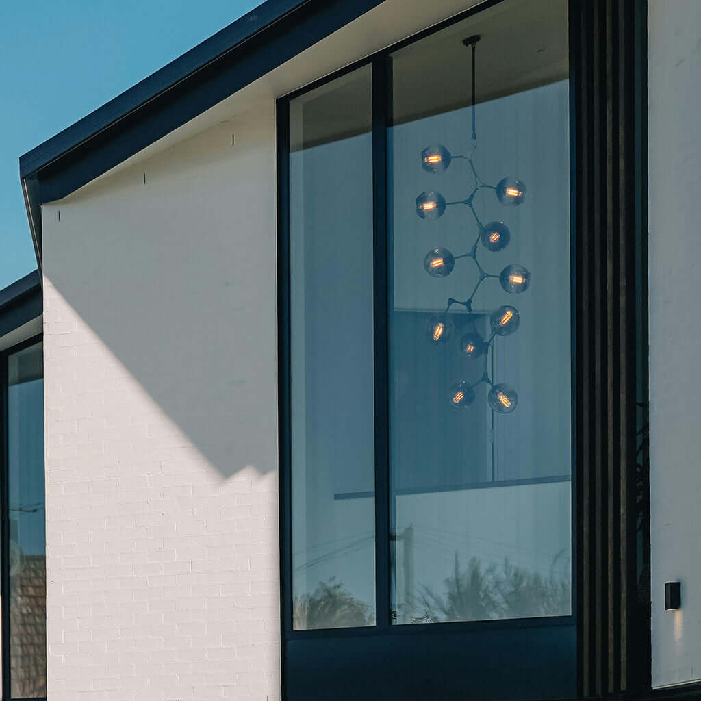 Modern building exterior with a chandelier inside reflected in large glass windows.