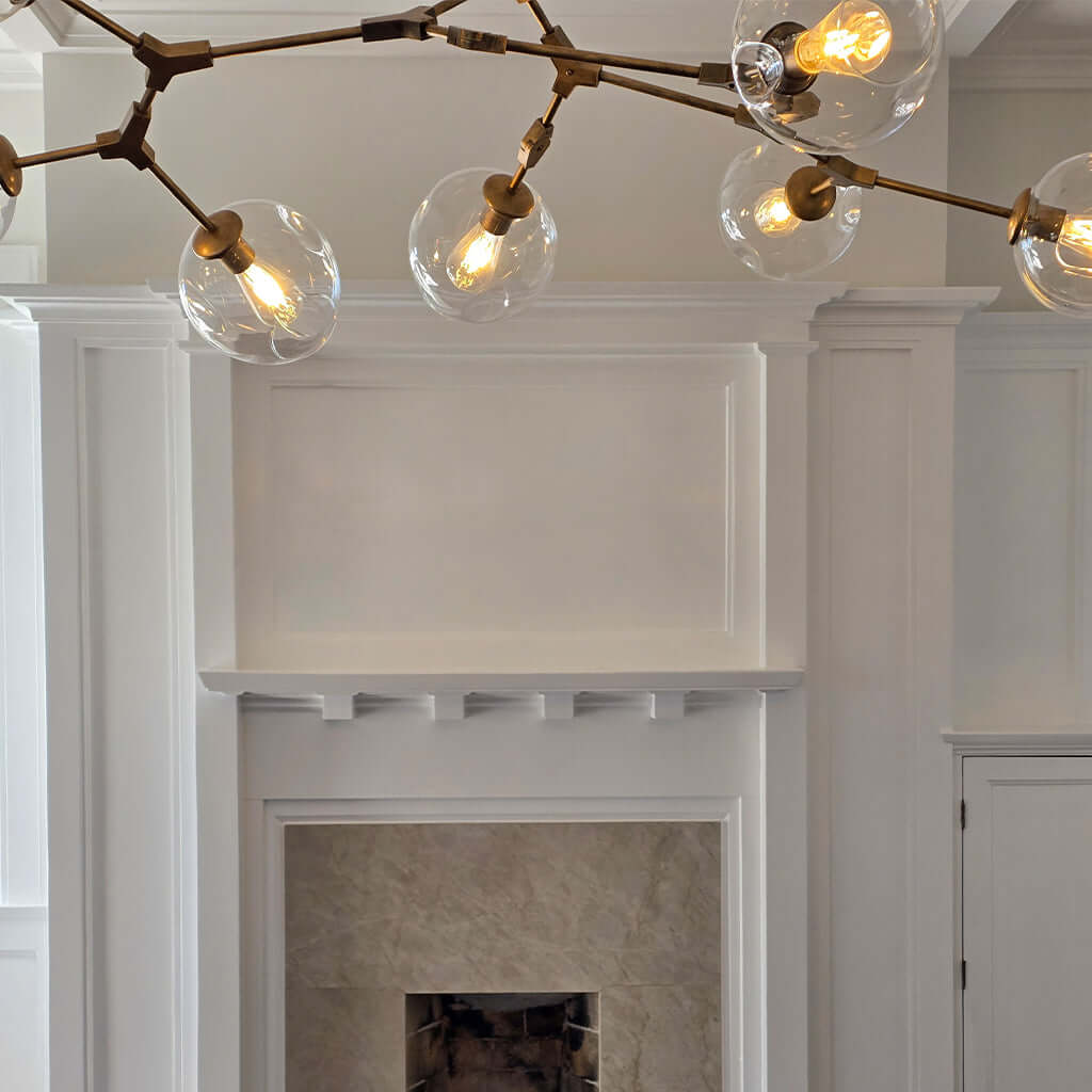 Modern chandelier with glass shades above a fireplace in a room with white walls.