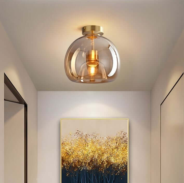 A Deon ceiling light with a tinted amber glass shade and brass fittings, installed in a room above a wall painting.