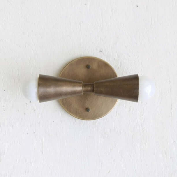 Brass wall sconce with two cylindrical shades on a white background