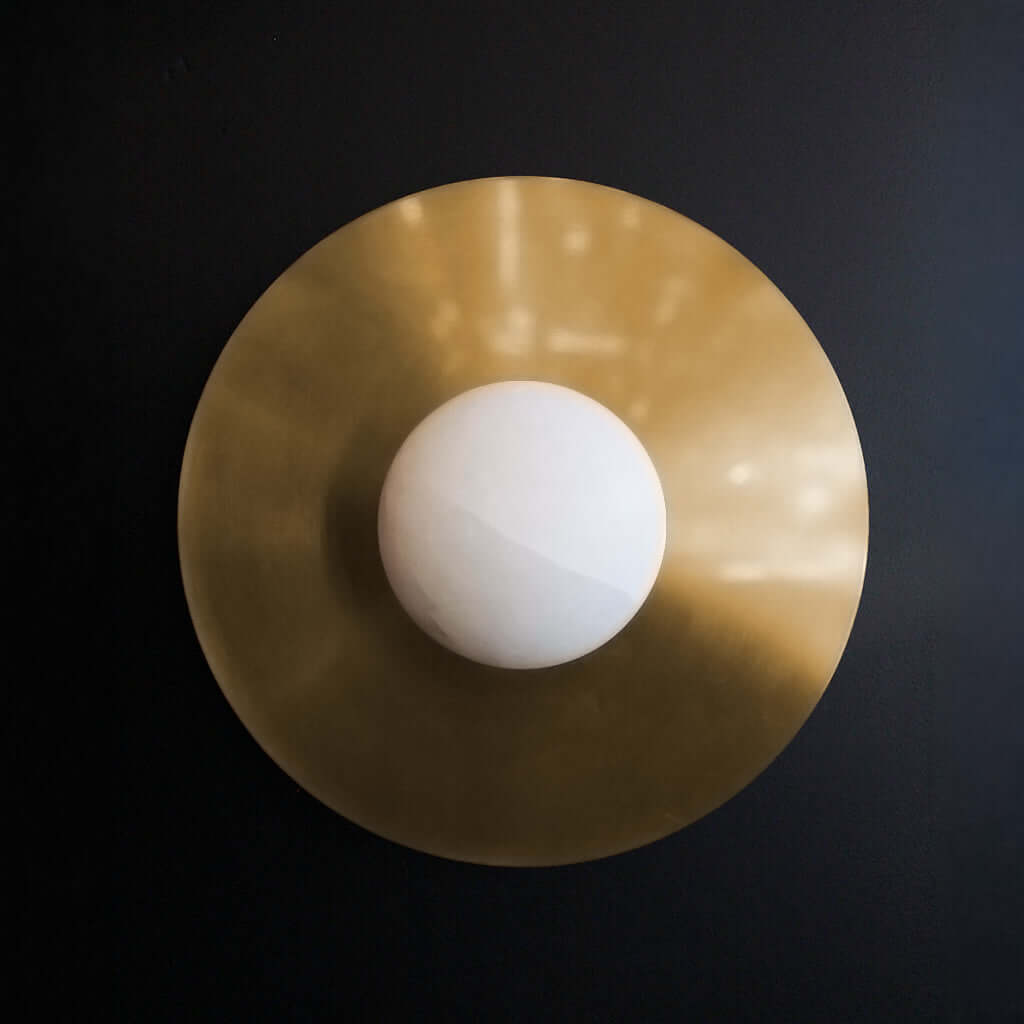 Gold circular wall light with a white stone sphere in the center on a black background