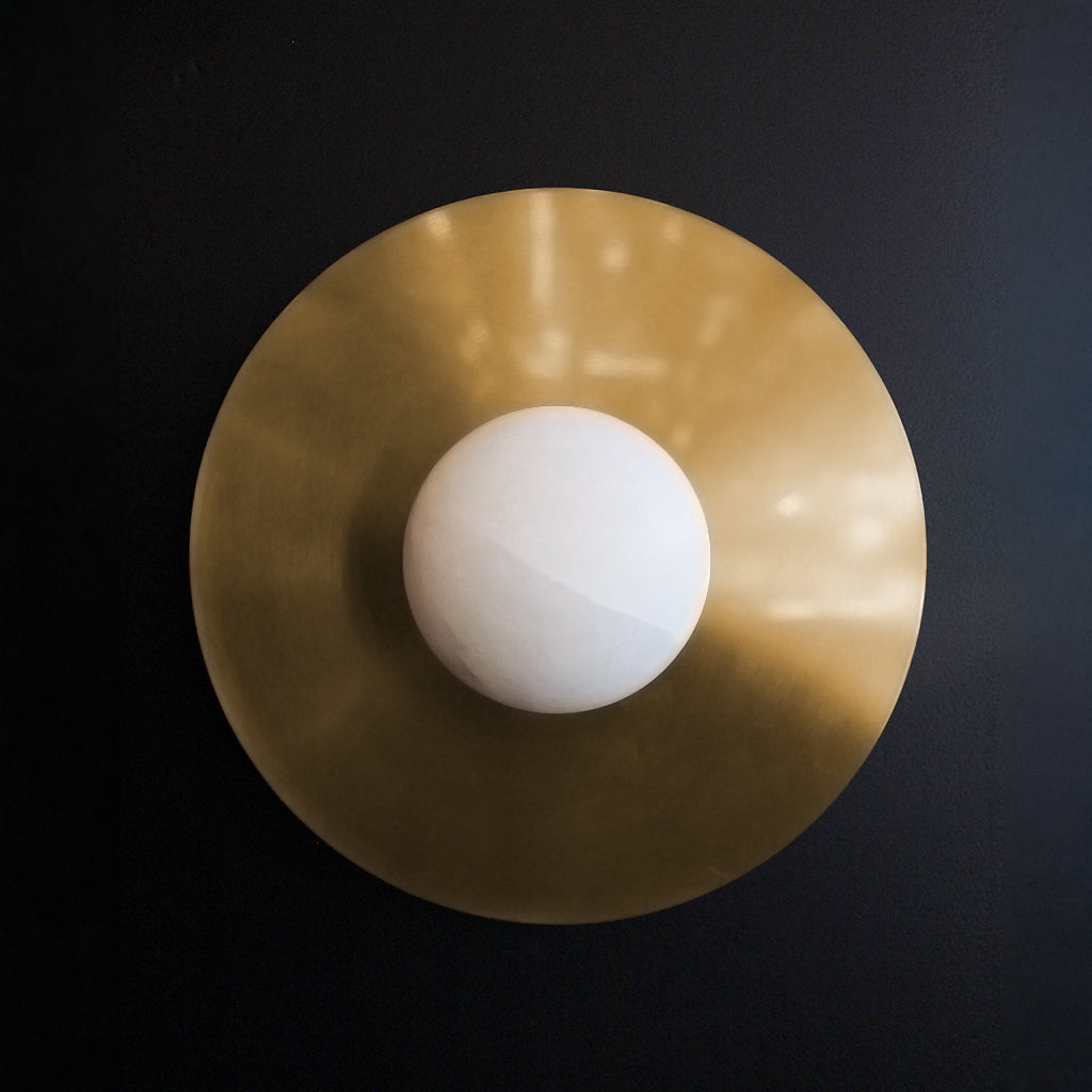 Gold circular wall light with a white stone sphere in the center on a black background
