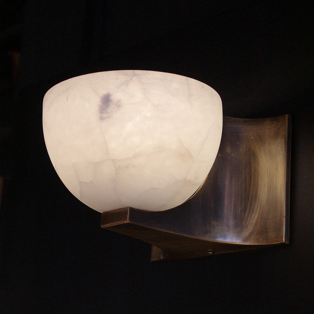 Wall-mounted light fixture with a white marble-like shade on a dark background