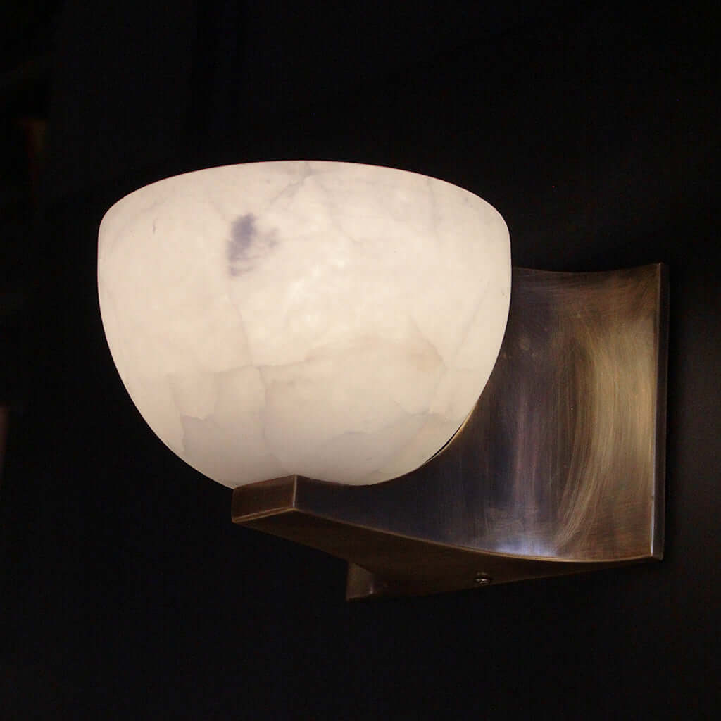 Wall-mounted light fixture with a white marble-like shade on a dark background