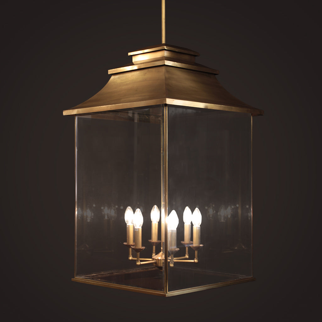 Brass lantern style pendant light with tiered top and glass panels against dark background