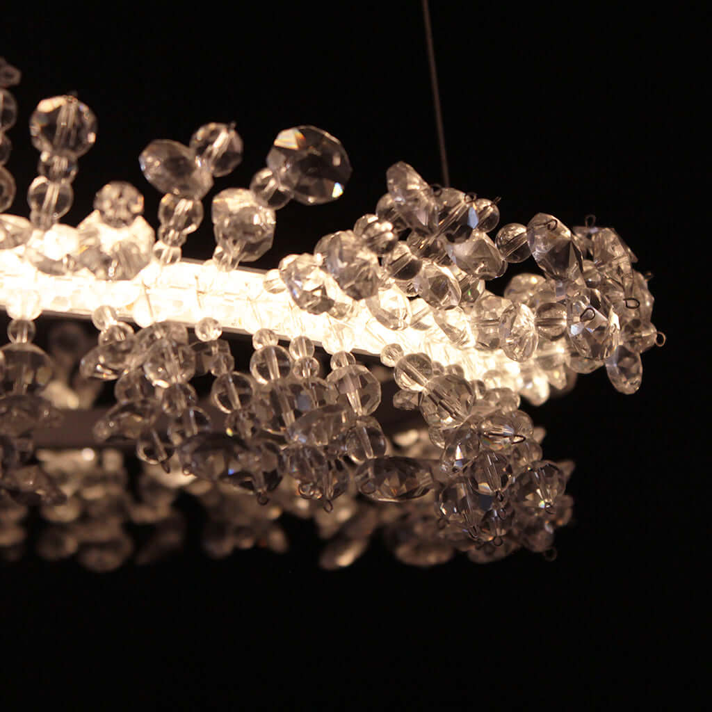 A close-up of a modern chandelier featuring a glowing white curved frame adorned with numerous clear faceted crystal beads and clusters, set against a solid black background.
