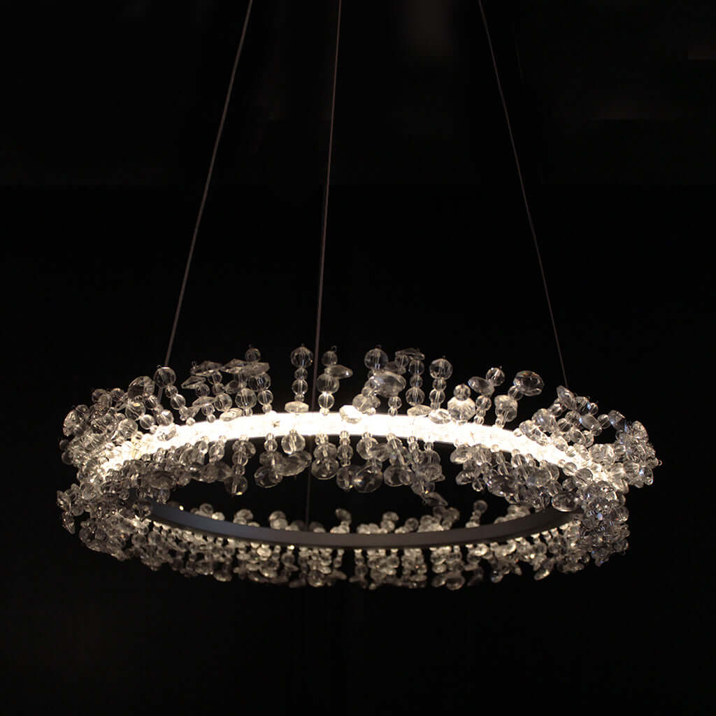 A modern circular LED chandelier with clear crystal beads, suspended against a solid black background.