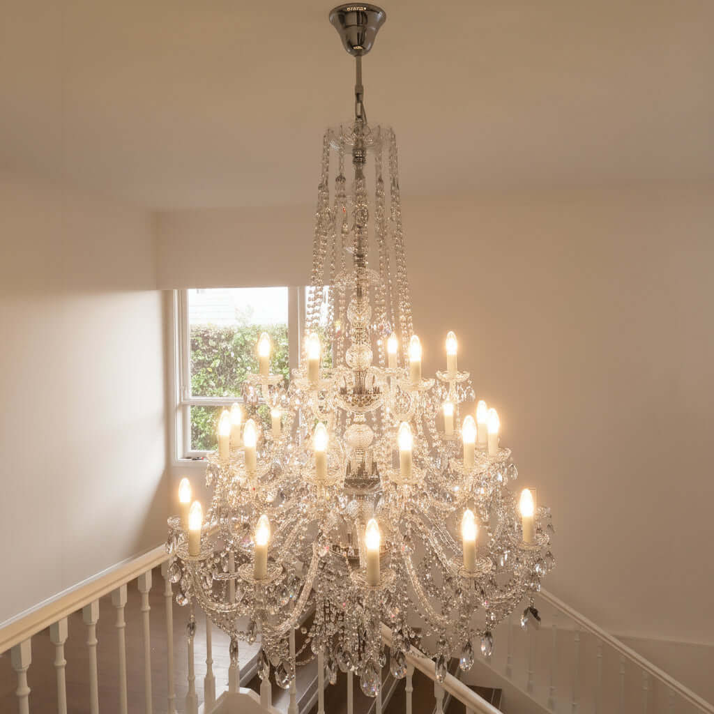 Crystal chandelier hanging in a room with a window and staircase.
