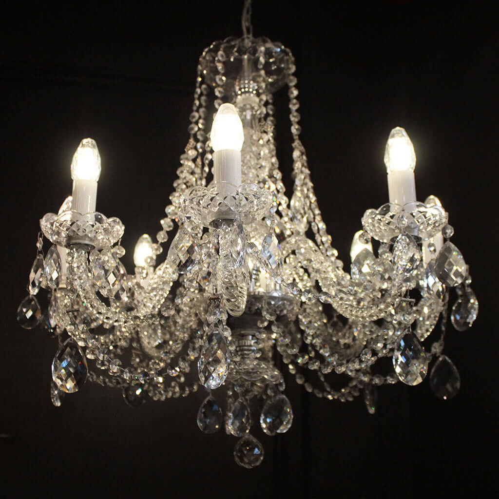 An eight-light crystal chandelier with clear faceted crystal beads, teardrop pendants, and candle-style bulbs turned on against a black background.