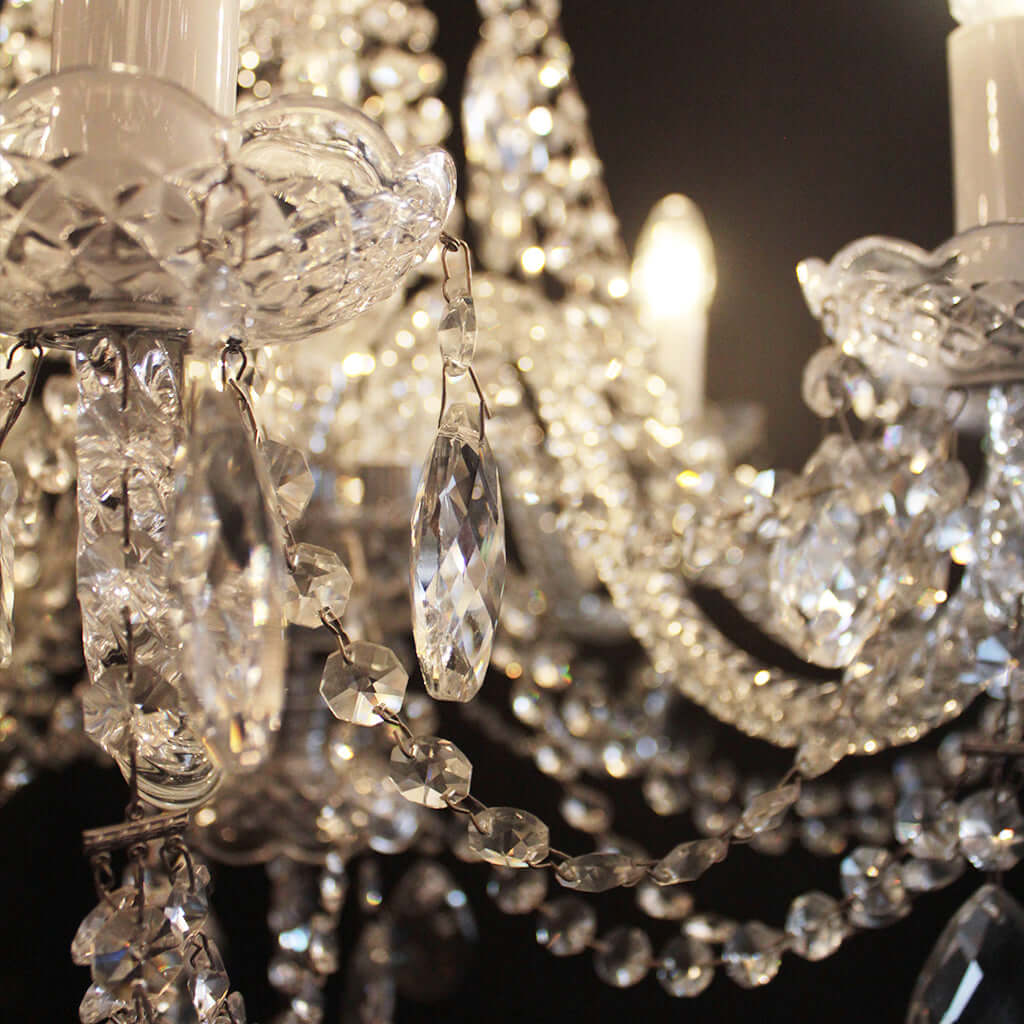 Close-up of a crystal chandelier with faceted clear crystal drops, bead strands, and lit candle-style bulbs against a dark background.
