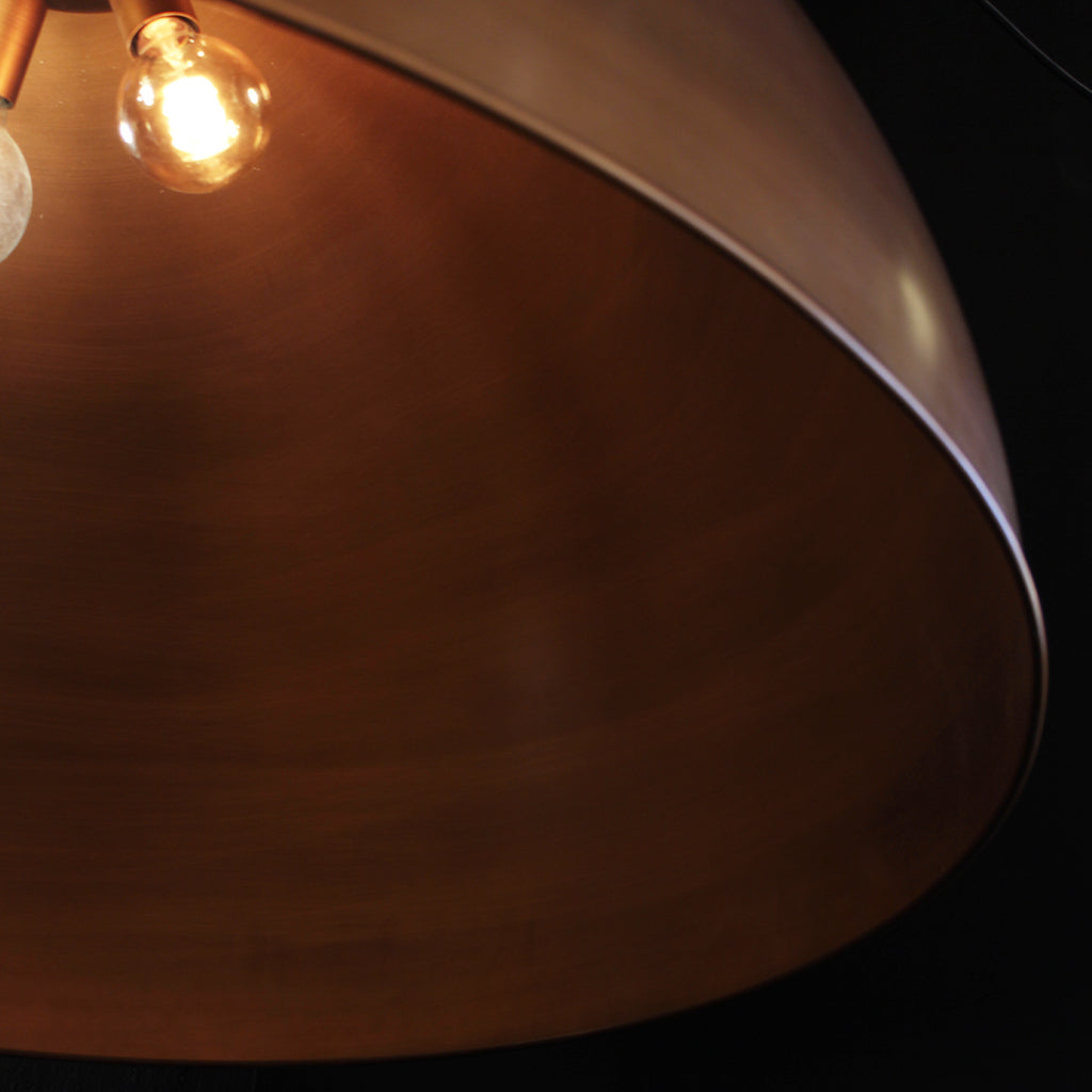 Close-up of a large dome-shaped pendant light with a warm metallic bronze interior and a glowing exposed bulb inside, set against a dark background.