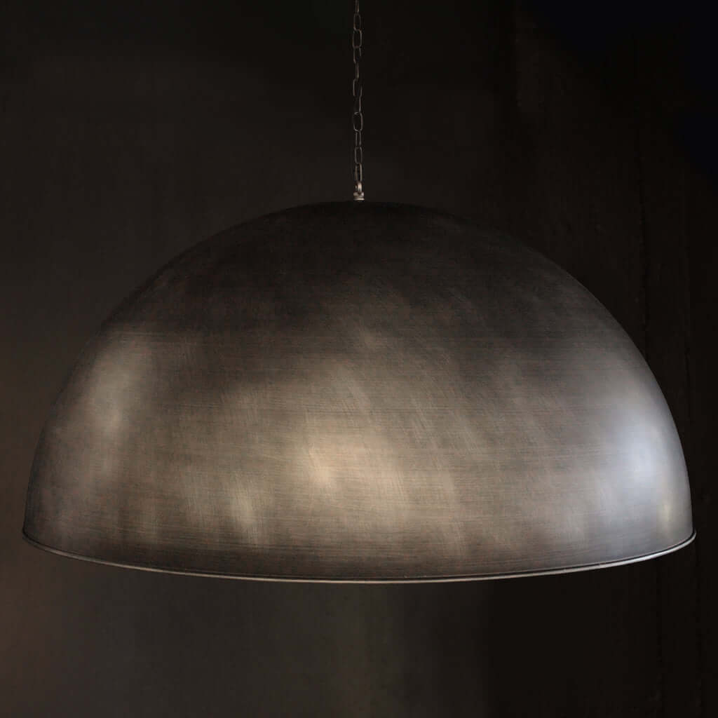 A large dome-shaped pendant light with a textured, brushed dark silver metallic finish, suspended by a thin chain against a dark background.