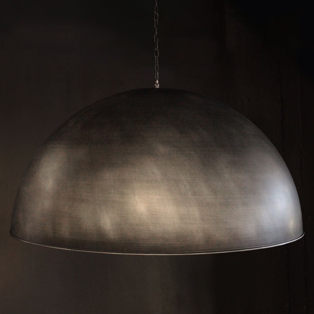 A large dome-shaped pendant light with a brushed metallic silver finish, suspended by a chain against a dark background.
