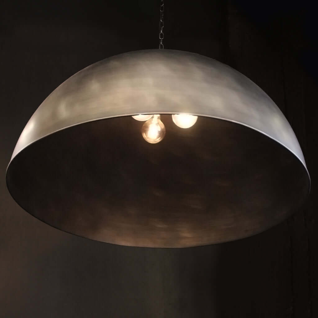 A large dome-shaped pendant light with a brushed silver metallic finish, shown illuminated against a dark background.