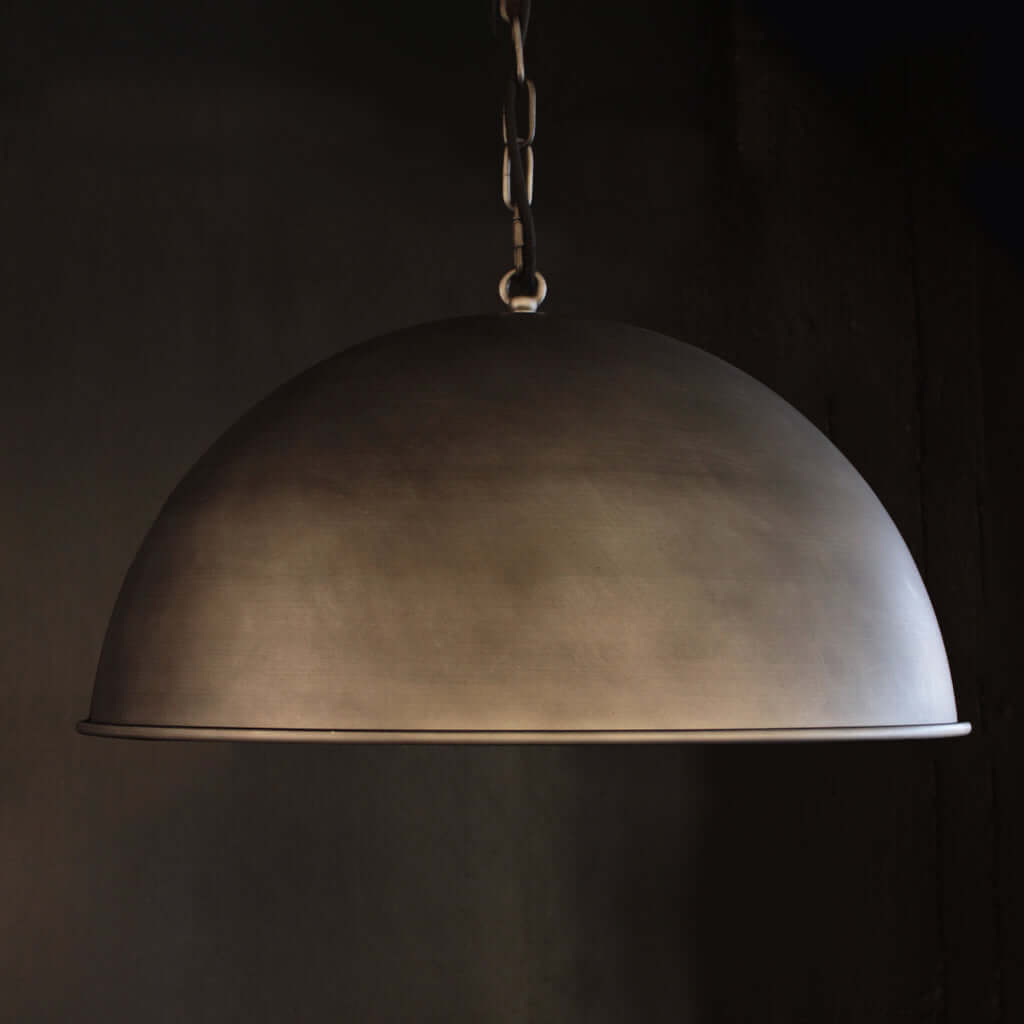 A dome-shaped pendant light with a dark, textured metallic finish hanging from a chain against a dark background.
