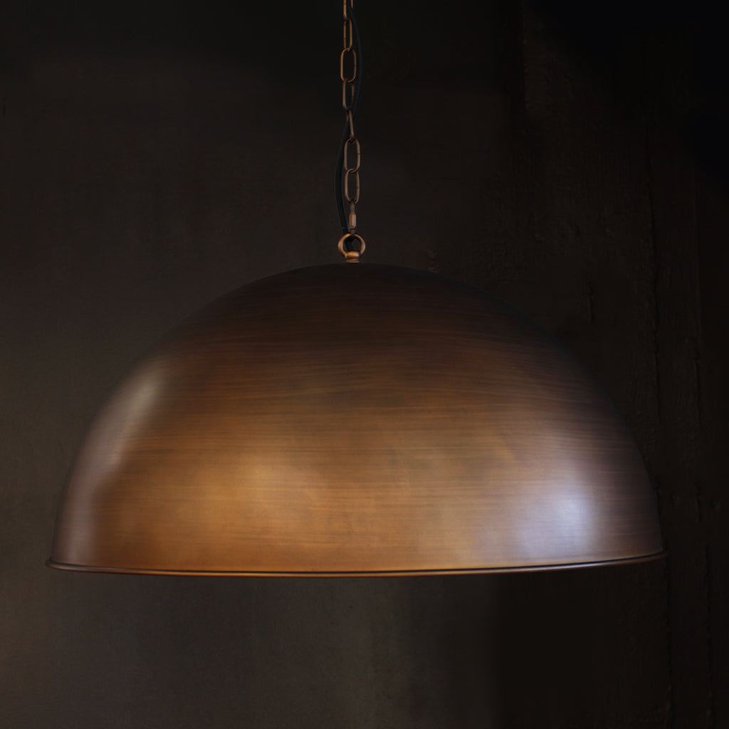 A dome-shaped pendant light with a brushed brass bronze metal shade hanging from a chain against a dark background.