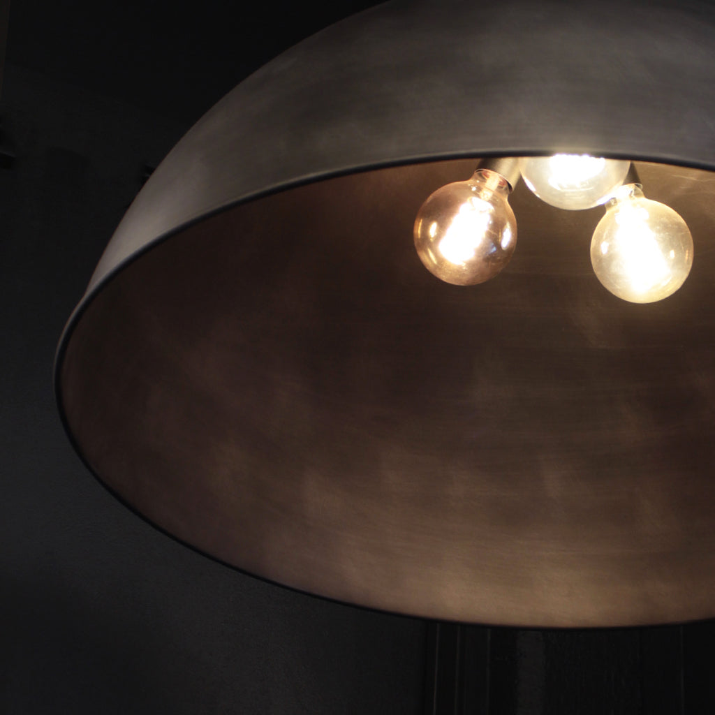 A close-up of a dome-shaped pendant light fixture with a dark silver metallic finish and three glowing warm Edison-style bulbs visible inside.