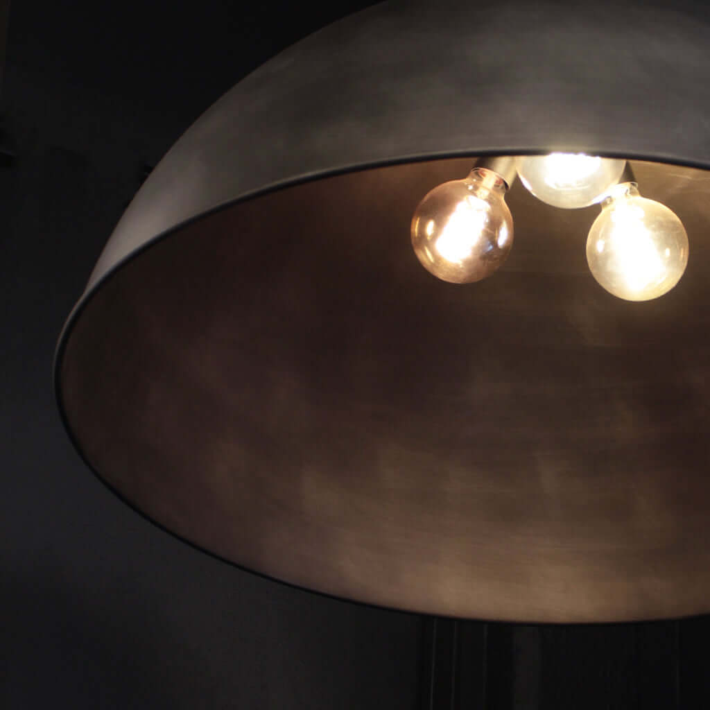 A close-up of a dome-shaped pendant light fixture with a dark silver metallic finish and three glowing warm Edison-style bulbs visible inside.