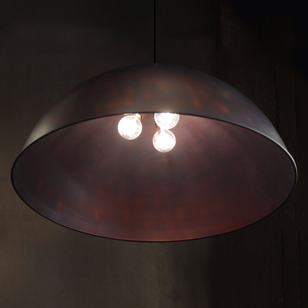 A large dome-shaped pendant light with a dark metallic bronze finish, housing three glowing warm white light bulbs against a dark background.