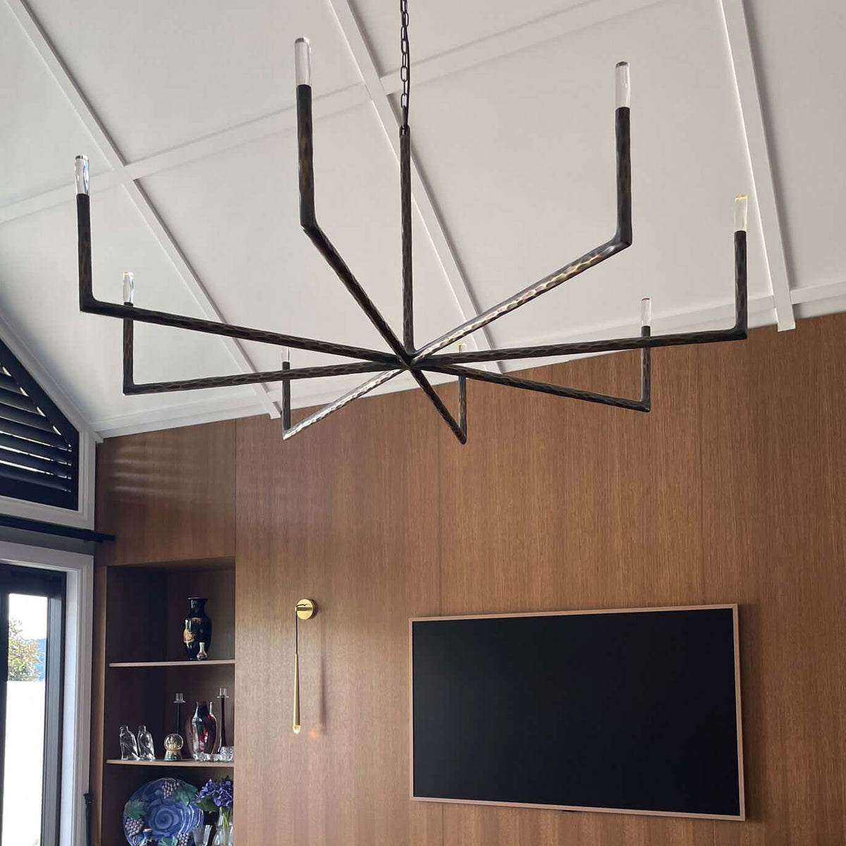 Modern chandelier hanging in a room with wooden walls and a television.