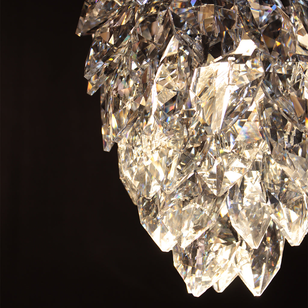 A close-up of a clear faceted crystal chandelier against a solid black background, showing multiple layered geometric crystal prisms with bright reflections.
