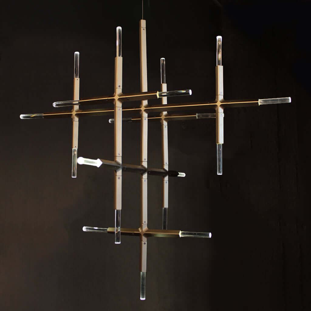 A modern multi-arm chandelier with clear crystal cylindrical tubes and warm brass-finished rods, suspended against a dark background.