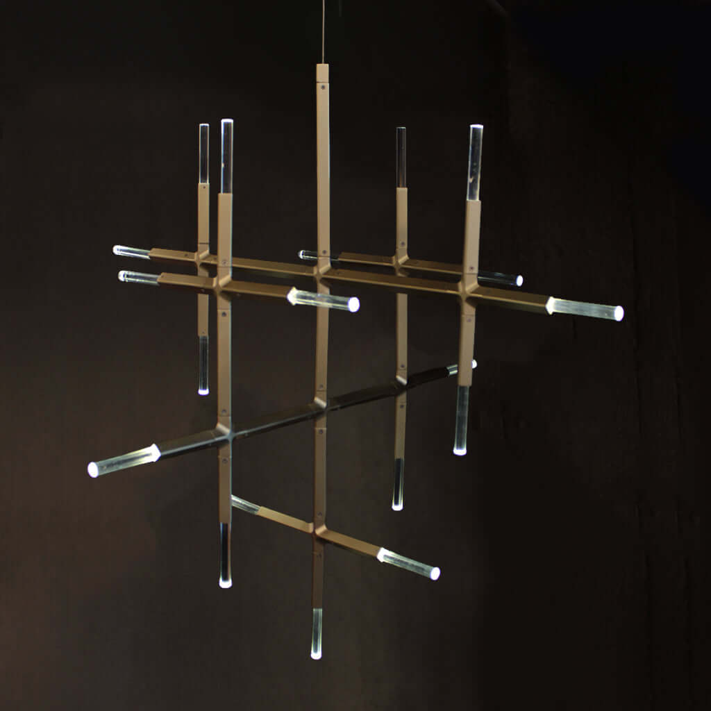 A modern chandelier with a gold-toned geometric metal frame and clear crystal cylindrical tubes, suspended against a dark background.
