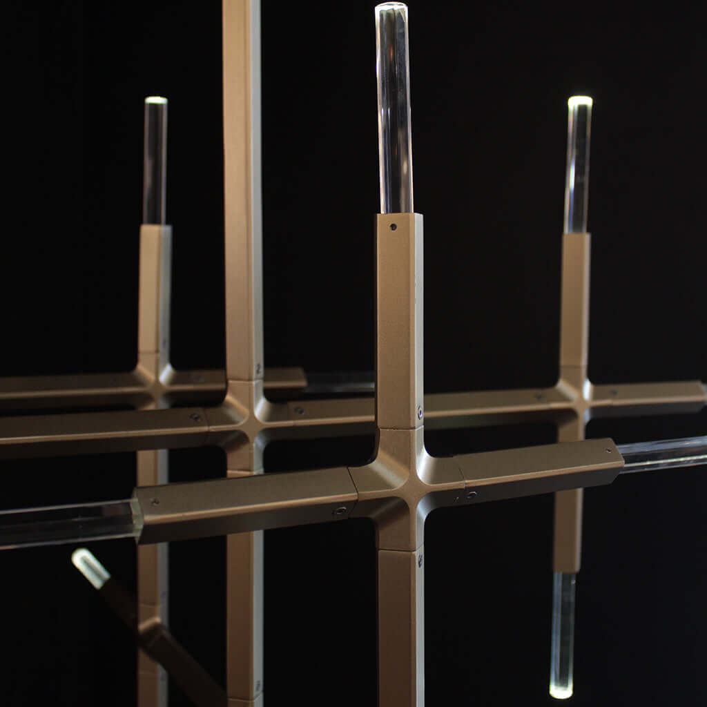 A modern chandelier with a brushed gold metal frame and clear crystal cylindrical shades, shown against a solid black background.