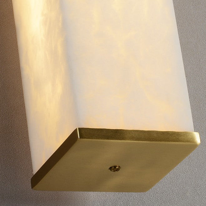 Wall-mounted light fixture with marble-like finish and gold base on a gray wall.