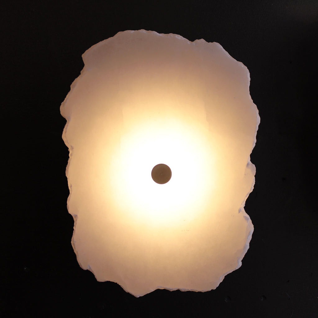 Wall sconce with glowing white stone and brass detail with dark background