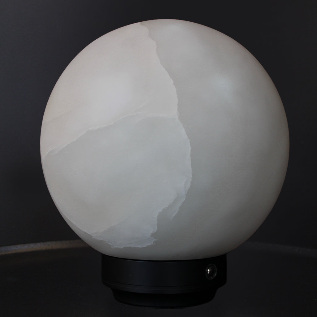 A spherical white alabaster lamp shade with natural veining, mounted on a black metal base against a dark background.