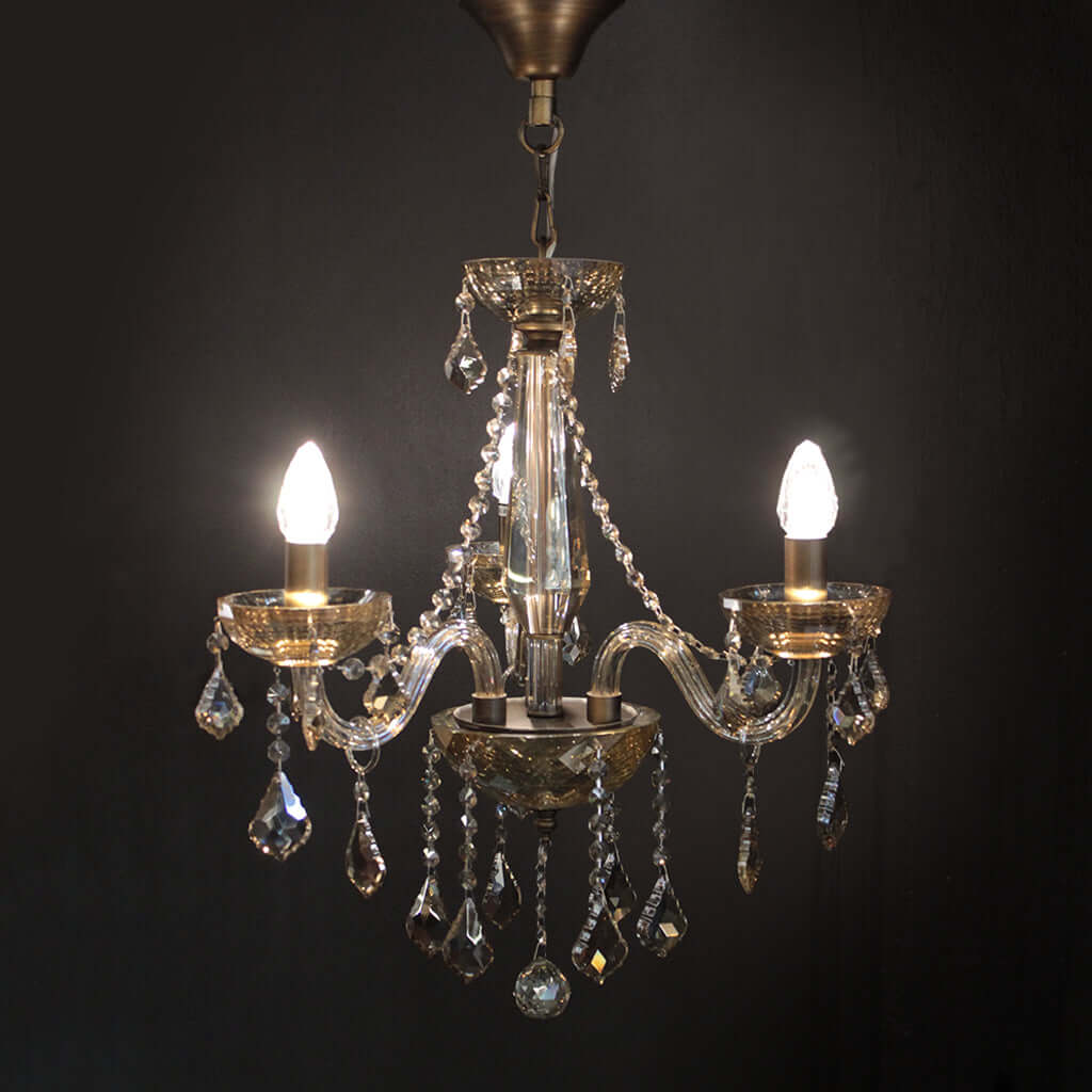 Crystal chandelier with three lit bulbs against a dark background