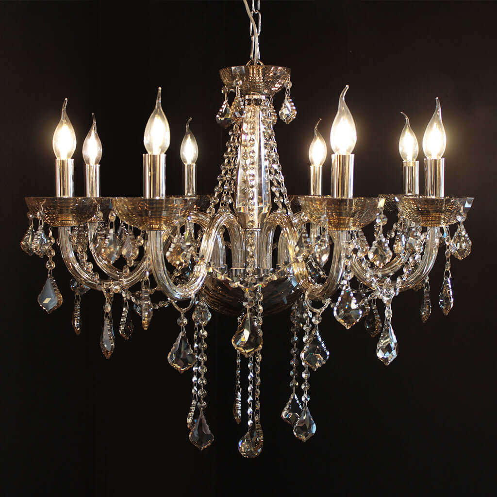 A multi-arm crystal chandelier with a polished chrome-toned metal frame and hanging warm glass teardrop prisms, shown illuminated against a black background.