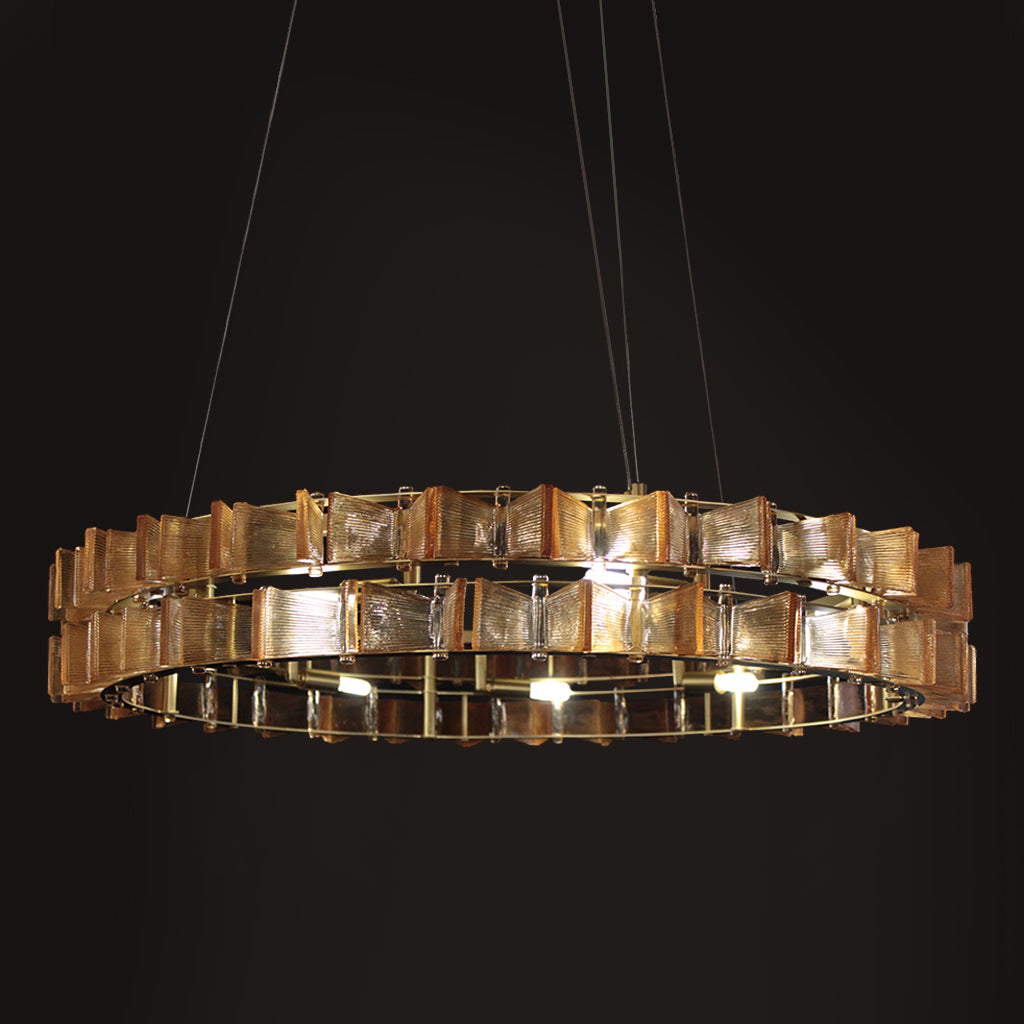 A modern circular chandelier with multiple tiers of textured, gold square glass panels, suspended by thin cables against a solid black background.