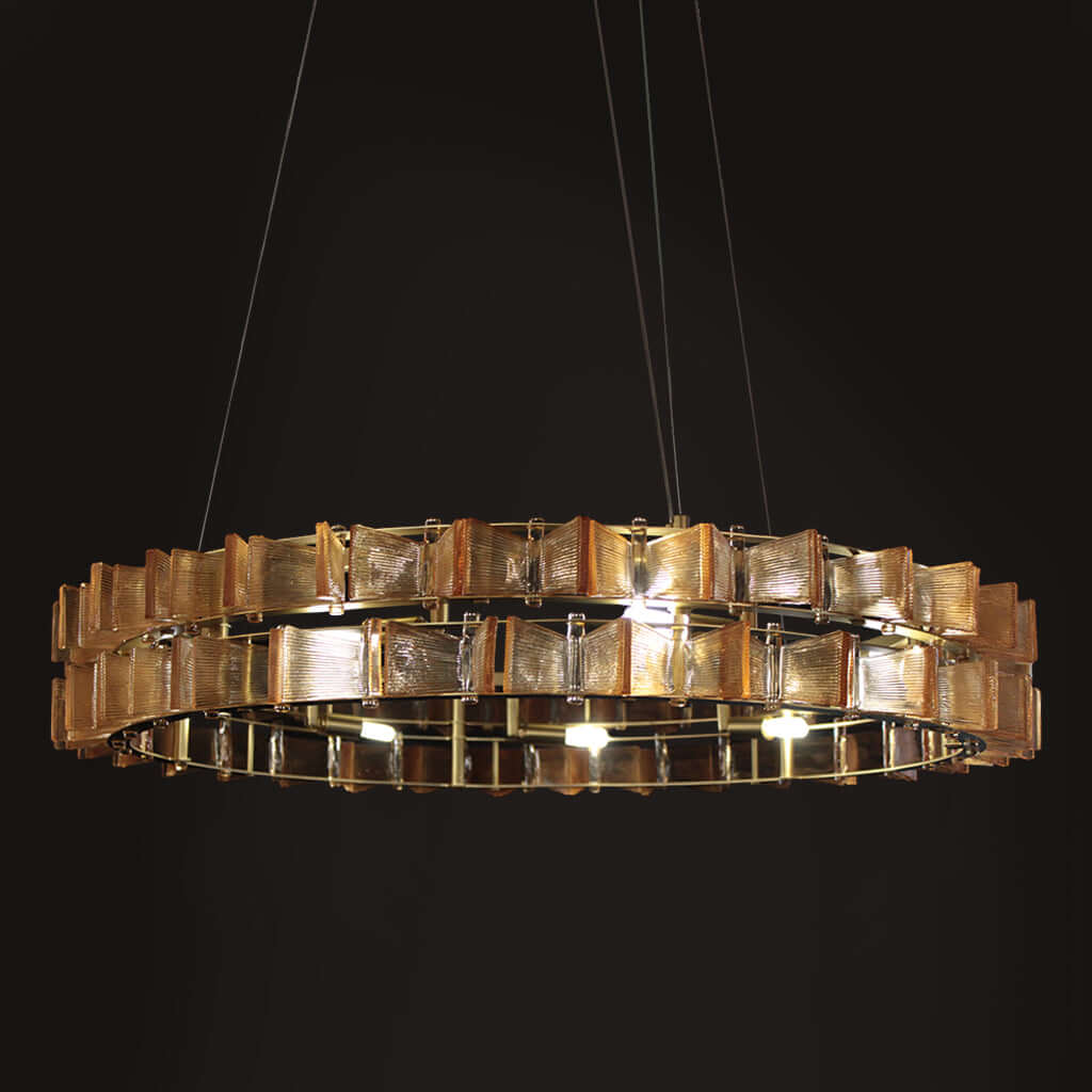A modern circular chandelier with multiple tiers of textured, gold square glass panels, suspended by thin cables against a solid black background.