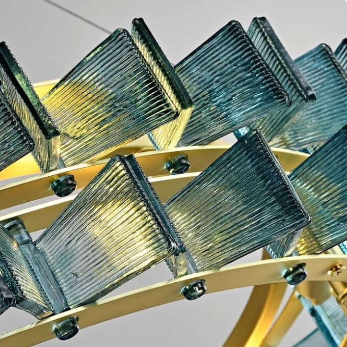 A close-up of a modern chandelier with rectangular blue glass shades featuring a textured, ribbed pattern and a warm metallic gold finish, set against a dark background.