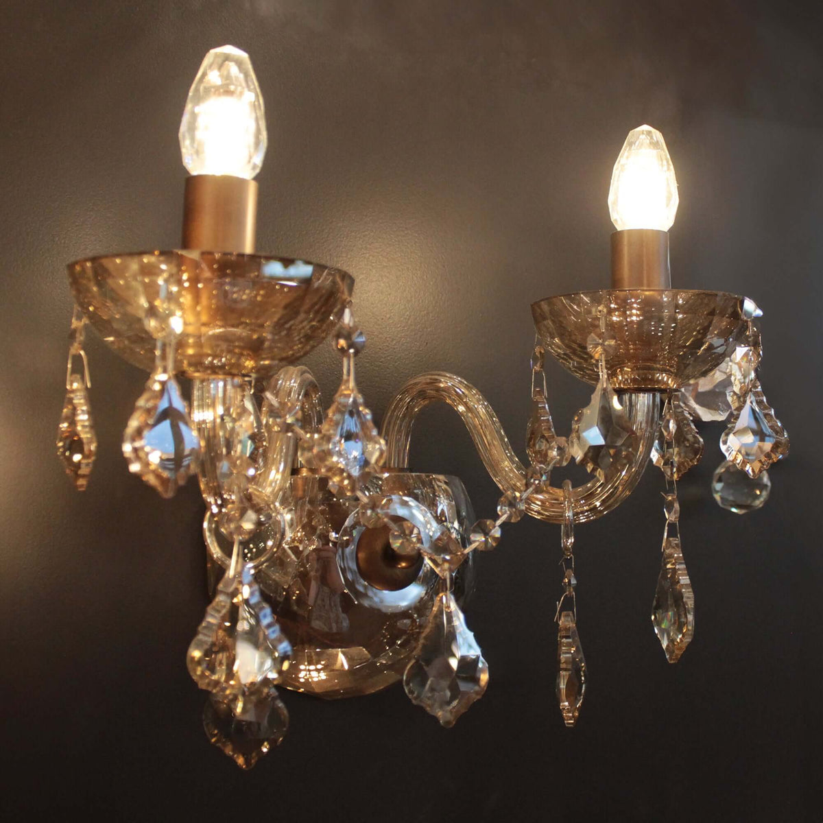 Decorative wall sconce with crystal accents and two lit light bulbs on a dark background.