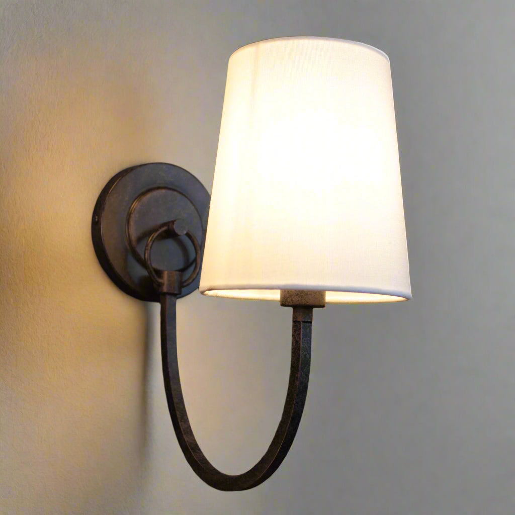 Wall-mounted lamp with a white shade and metal arm on a dark wall.