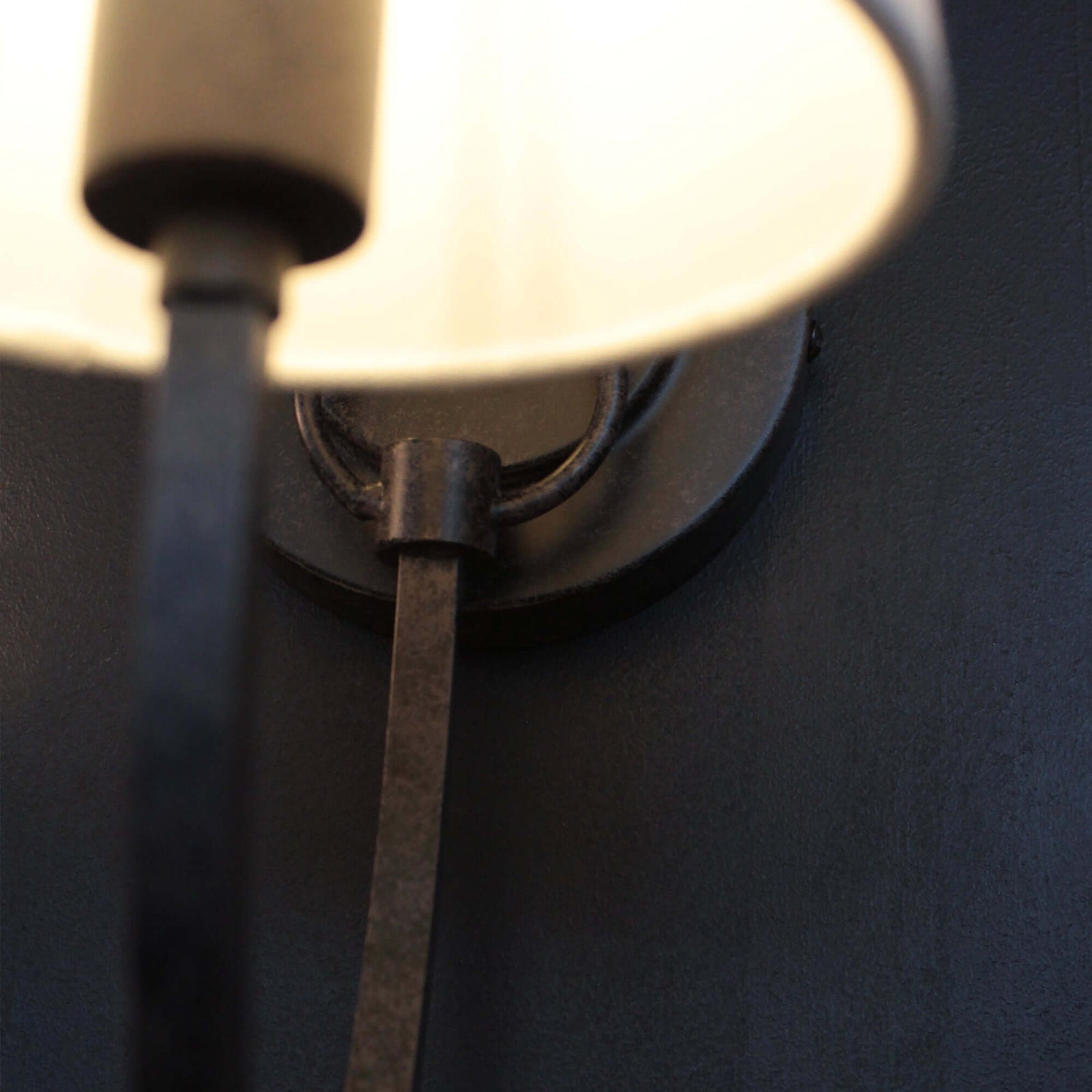 Wall-mounted lamp with a white shade and metal arm on a dark wall.