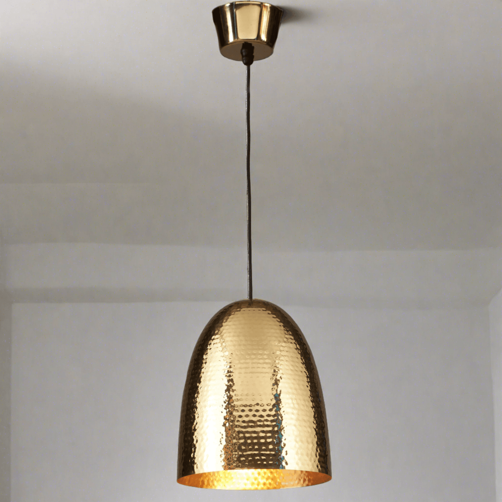 A tall domed pendant light with a brass base and a unique hammered metal texture, finished in gold color, suspended from the ceiling.