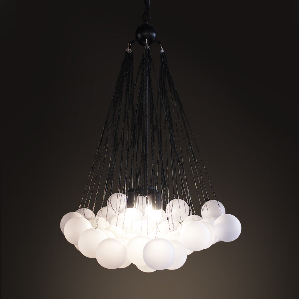 A modern chandelier with multiple white frosted glass globe shades suspended by thin black cords from a black ceiling canopy, shown against a dark background.