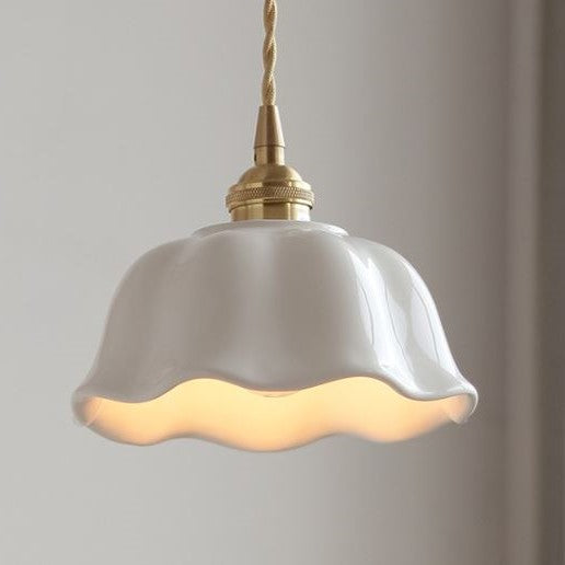 A white ceramic pendant light with a rippled design and brushed brass fittings, hanging against a soft-lit background.