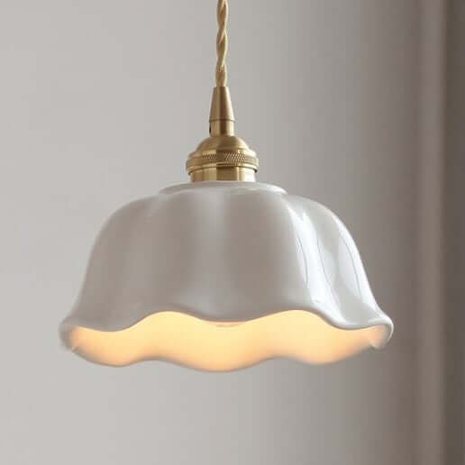 A white ceramic pendant light with a rippled design and brushed brass fittings, hanging against a soft-lit background.