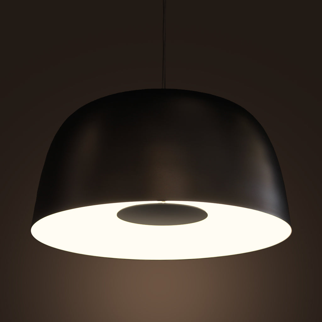 A modern dome-shaped pendant light with a matte black exterior and a glowing white interior, suspended against a dark brown background.