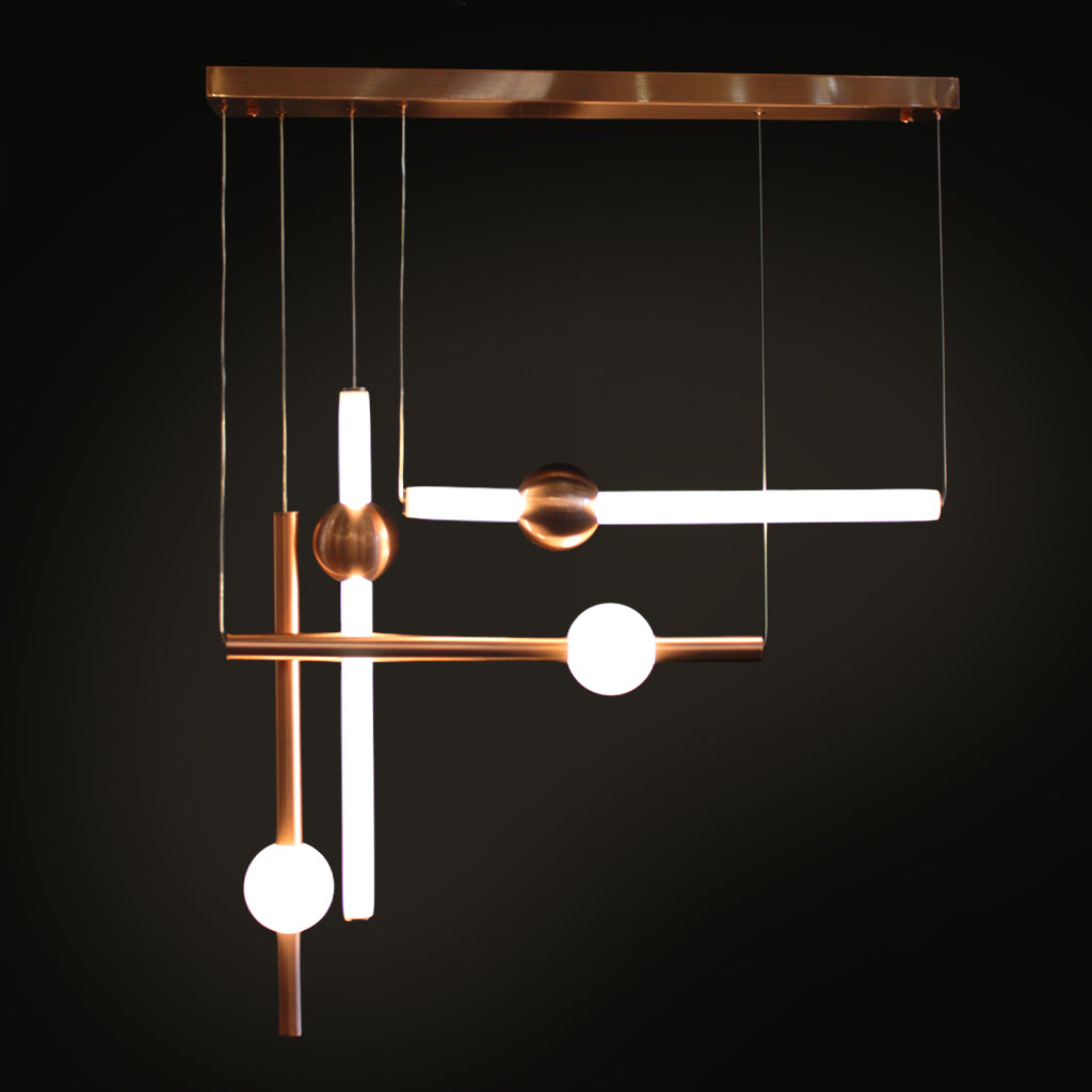 A modern geometric pendant light fixture with a brushed copper finish and glowing white glass spherical elements, suspended against a solid black background.