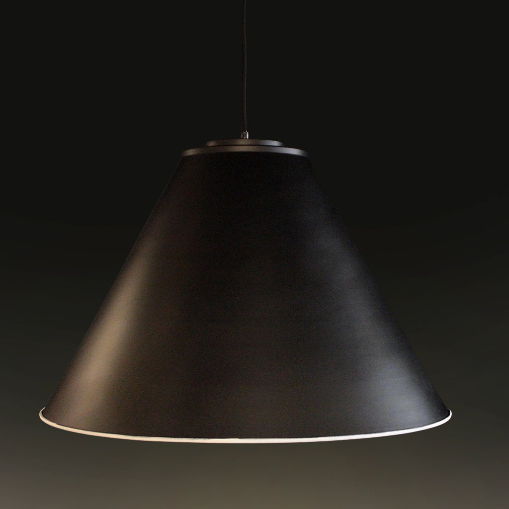 A black conical pendant light shade with a brushed metal top ring, suspended against a dark studio background.