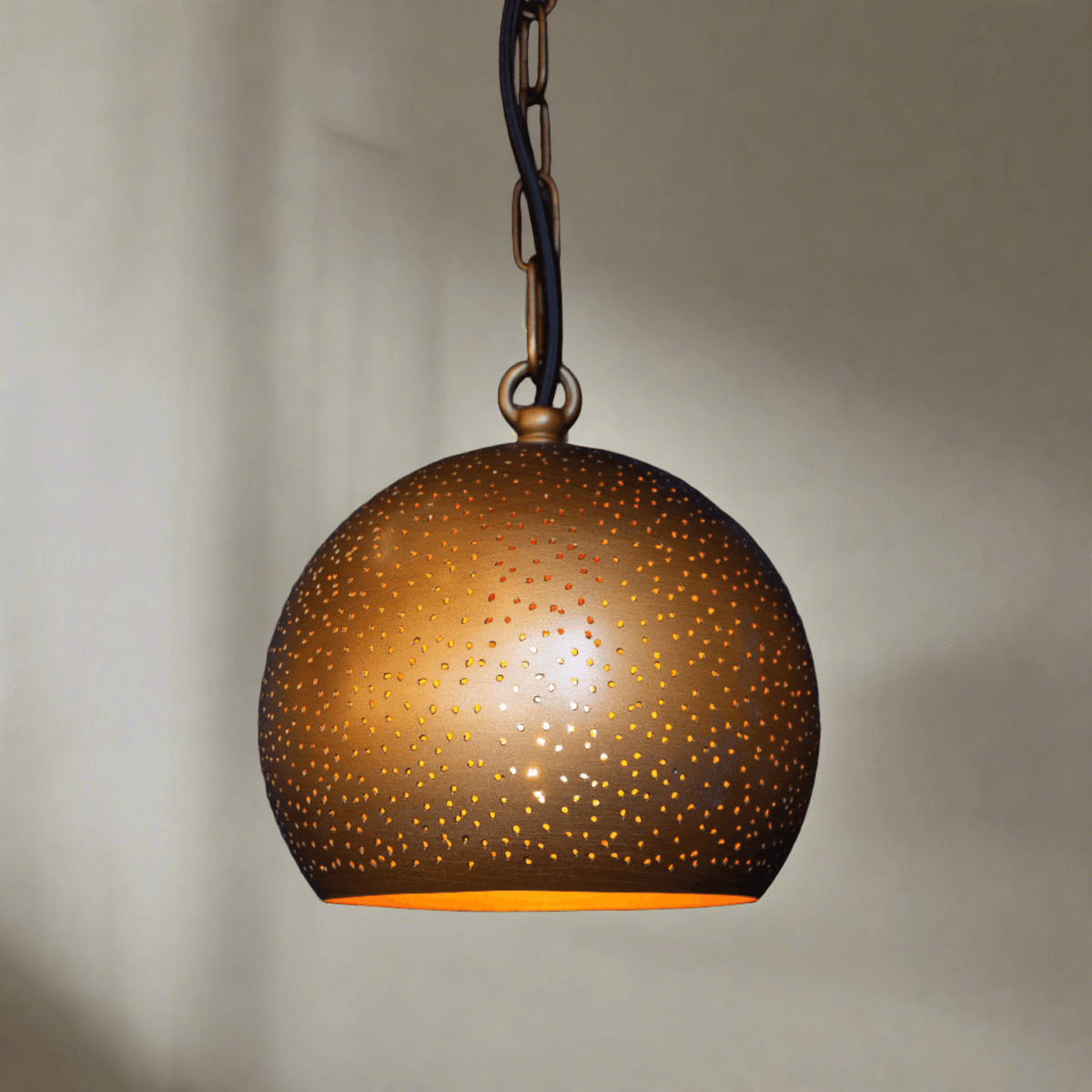 A Moroccan-inspired Yasmine pendant light with a rounded dome shade featuring perforations and an antique brass finish, hanging against a neutral background.