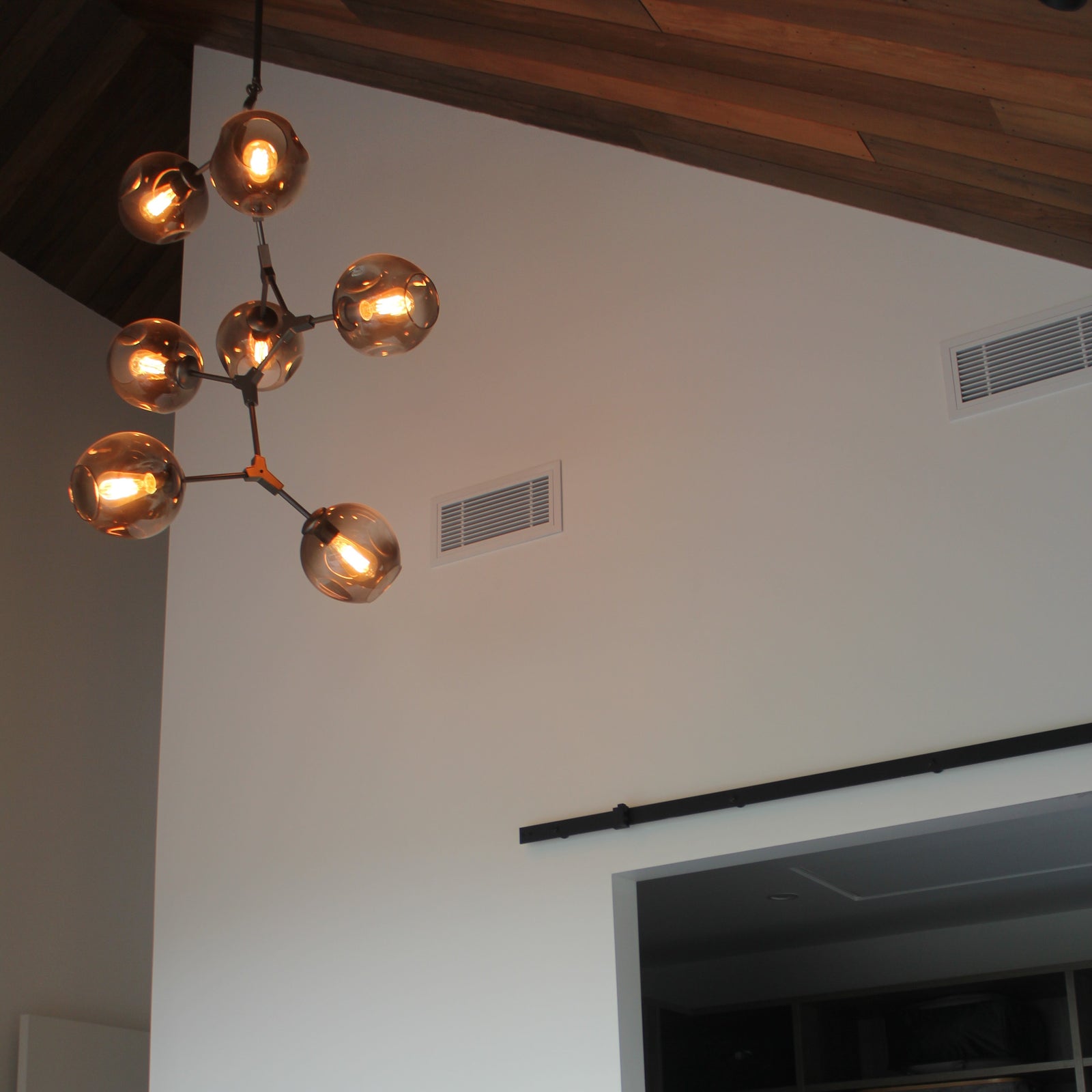 A vertical pendant light with multiple glass bulb covers in a warm hue, hanging from adjustable metal arms against a wooden ceiling.